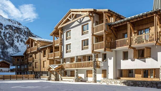 A multi-story wooden building with balconies, stone pillars, and a snowy mountain backdrop. - Spacious 3-Room Apartment with Balcony, Parking, and WiFi in Val-d'Isère (Val-d'Isère)