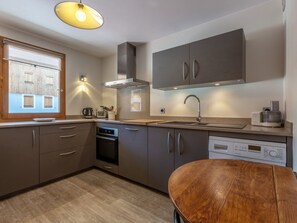 A modern kitchen with built-in appliances, a wooden dining table, and a window with blinds. - Spacious 3-Room Apartment with Balcony, Parking, and WiFi in Val-d'Isère (Val-d'Isère)
