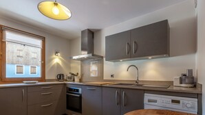 A modern kitchen with grey cabinets, a stainless steel range hood, a built-in dishwasher, and a wooden dining table. - Spacious 3-Room Apartment with Balcony, Parking, and WiFi in Val-d'Isère (Val-d'Isère)