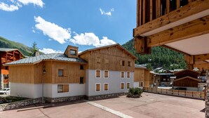 A traditional wooden building with a stone foundation, a courtyard, and a mountainous backdrop. - Spacious 3-Room Apartment with Balcony, Parking, and WiFi in Val-d'Isère (Val-d'Isère)