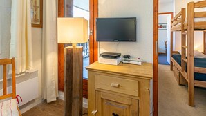 Ein Zimmer mit Holztisch, einem an der Wand befestigten Fernseher, Stockbetten, einem Sessel und einem Fenster mit Vorhängen.