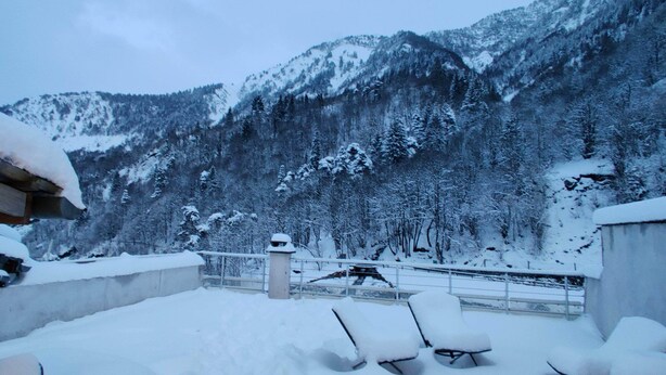 A snow-covered balcony with outdoor seating, overlooking a mountainous landscape.