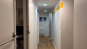 A narrow hallway with wooden flooring, white walls, and a door on the left.
