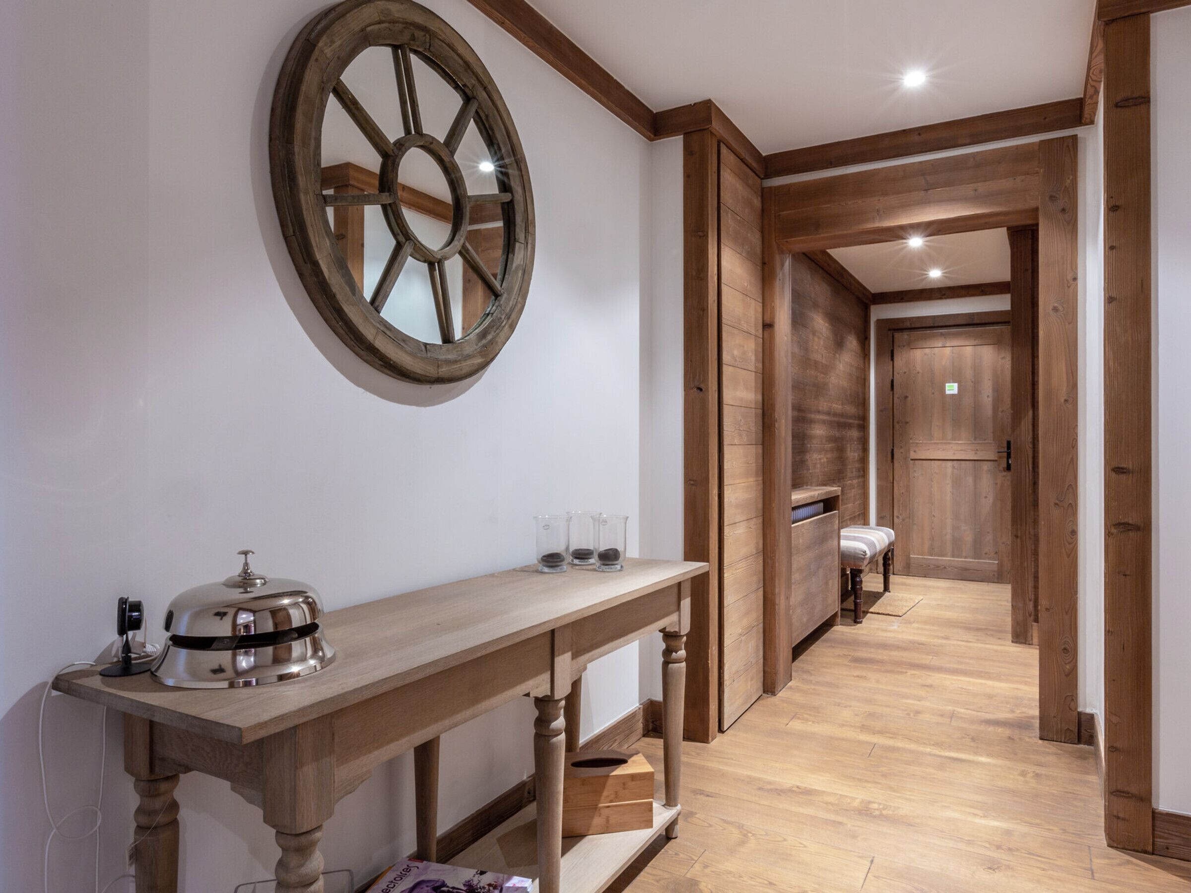 A hallway with a wooden table, a large mirror, and a door leading to another room.