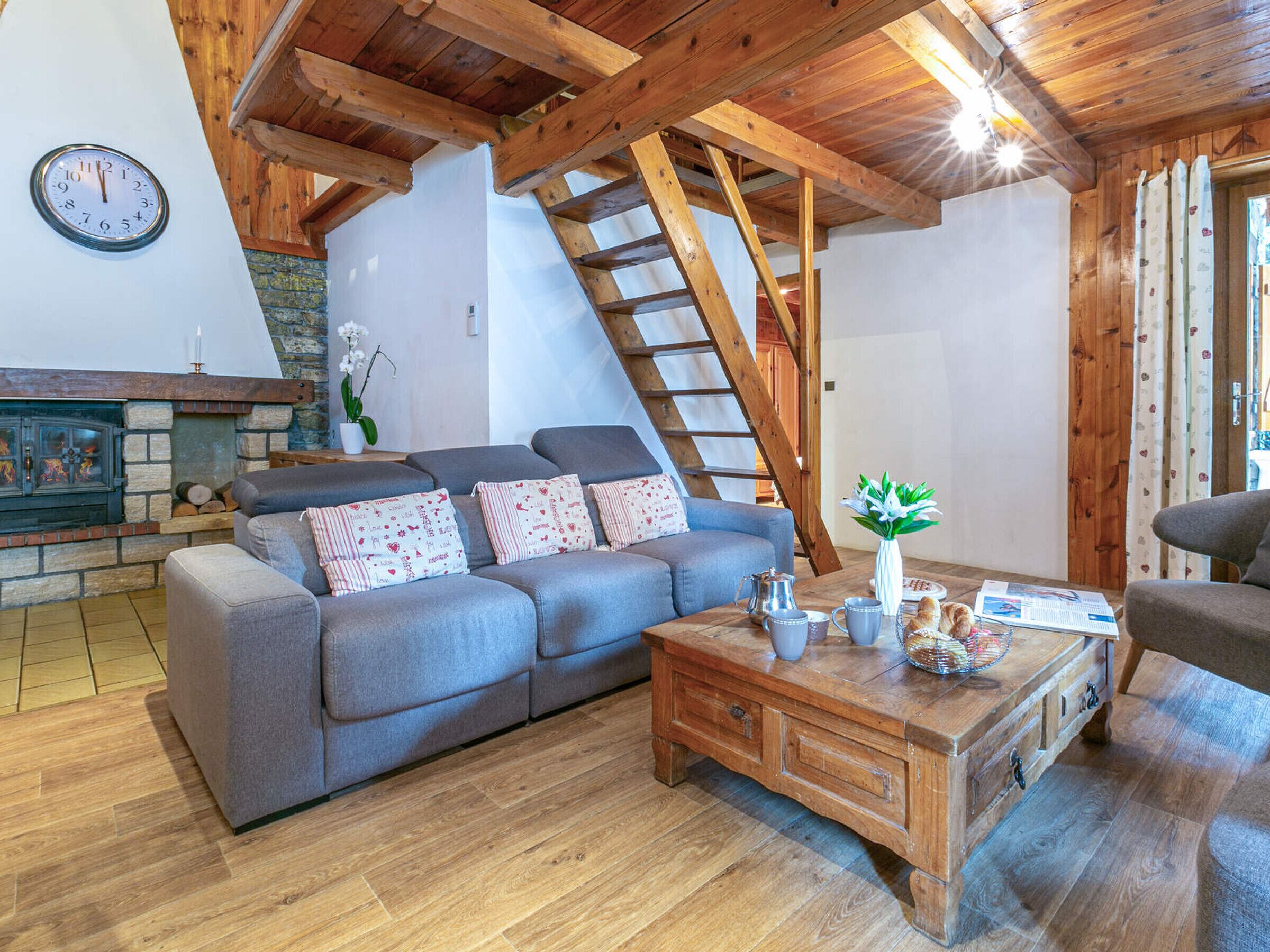 Una sala de estar acogedora con sofá, mesa de centro y chimenea. Se observa una escalera de madera al fondo.