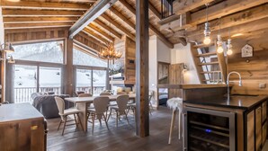 Un interior rústico de madera con comedor, cocina y vistas a un paisaje nevado.