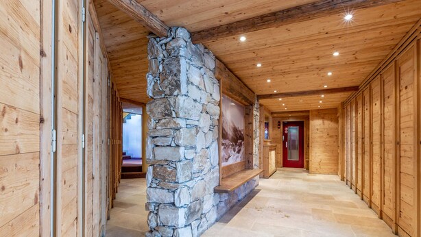 A hallway with wooden walls, a stone pillar, and a red door at the end. - Elegant 3-Room Apartment with Balcony in Central Val-d'Isère – Sleeps 6, Modern Amenities (Val-d'Isère)