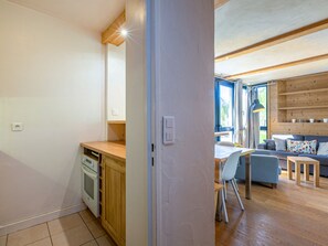 Een moderne keuken met houten kastjes en een ingebouwde oven, die uitkomt op een zithoek met een blauwe bank en houten vloeren.