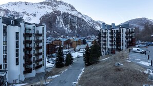 A snow-covered mountain town with modern multi-story buildings, a main road, and parked cars. - Elegant 3-Room Apartment with Balcony in Central Val-d'Isère – Sleeps 6, Modern Amenities (Val-d'Isère)