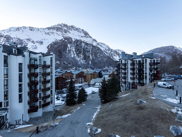 A snow-covered mountain town with modern multi-story buildings, a main road, and parked cars.