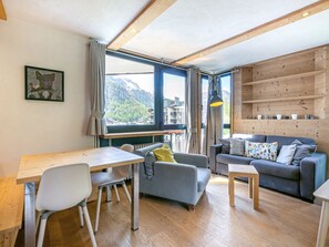 Un salon moderne avec un plancher en bois, un canapé, une table à manger avec des chaises et une grande fenêtre donnant sur les montagnes.
