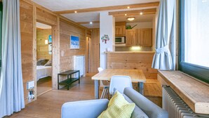 A cozy cabin interior with a wooden dining area, a sofa with a cushion, and a kitchen with wooden cabinets and a microwave. - Elegant 3-Room Apartment with Balcony in Central Val-d'Isère – Sleeps 6, Modern Amenities (Val-d'Isère)