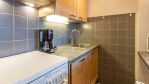 A compact kitchen with a white stove, a coffee maker, and wooden cabinets. - Charming 2-room apartment with pets allowed (Val-d'Isère)