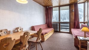 A cozy cabin interior with a wooden dining table, chairs, a sofa, and a window with a view of a snowy landscape. - Charming 2-room apartment with pets allowed (Val-d'Isère)