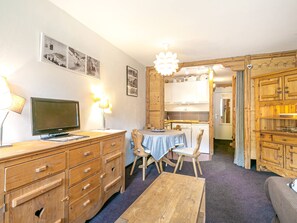 A compact living space with a wooden dining table, a TV, and a kitchenette.