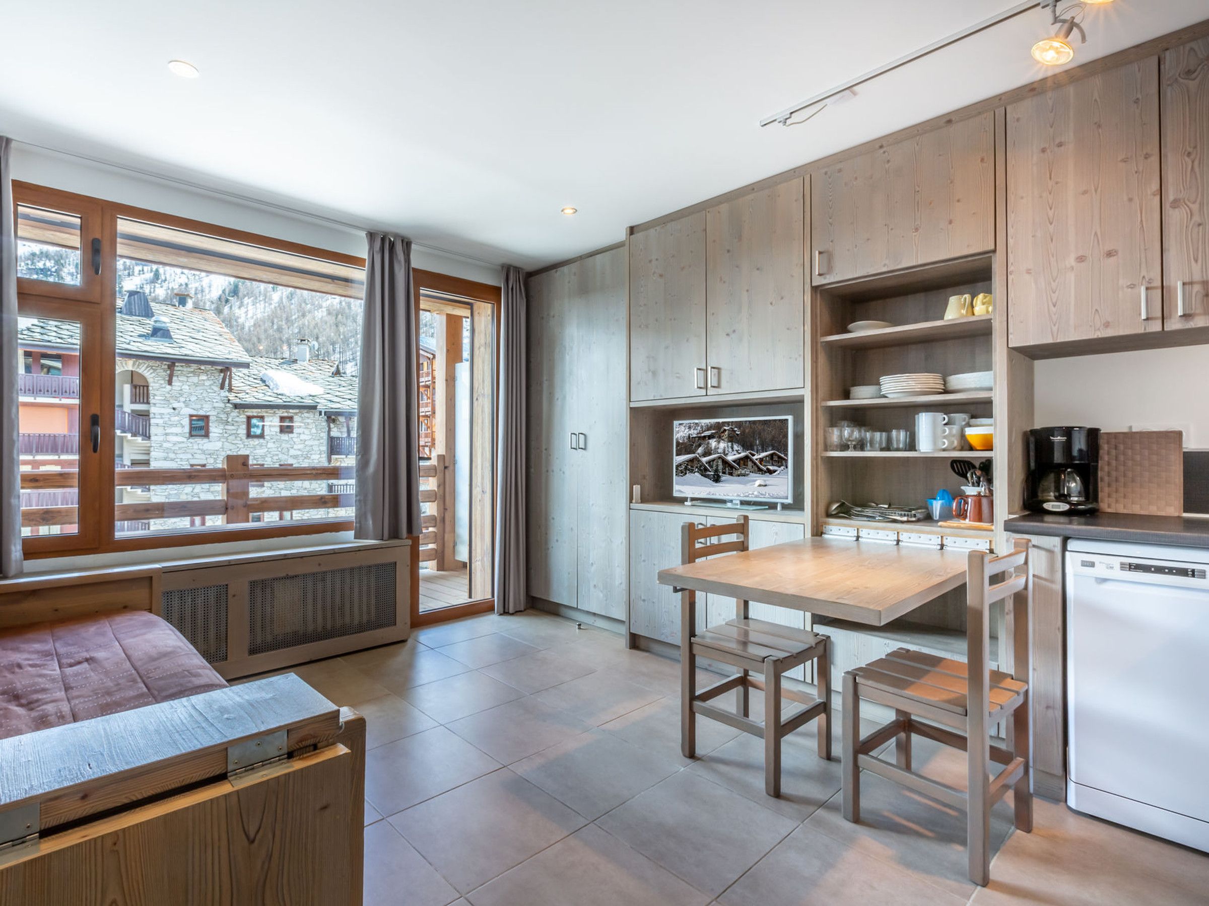 Een moderne keuken met houten kastjes, een eettafel en uitzicht op een besneeuwde berg.