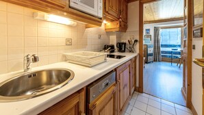 A kitchen with wooden cabinets, a stainless steel sink, a microwave, and a dishwasher. - Cozy Studio with Wifi in Central Location, Close to Slopes, Pets Welcome (Val-d'Isère)