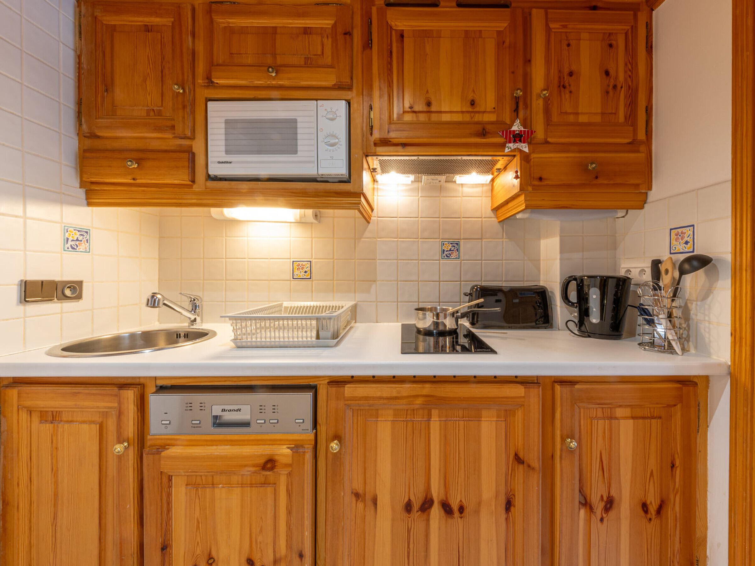 Une cuisine avec des meubles de rangement en bois, un four à micro-ondes, un grille-pain, un évier et un égouttoir à vaisselle.