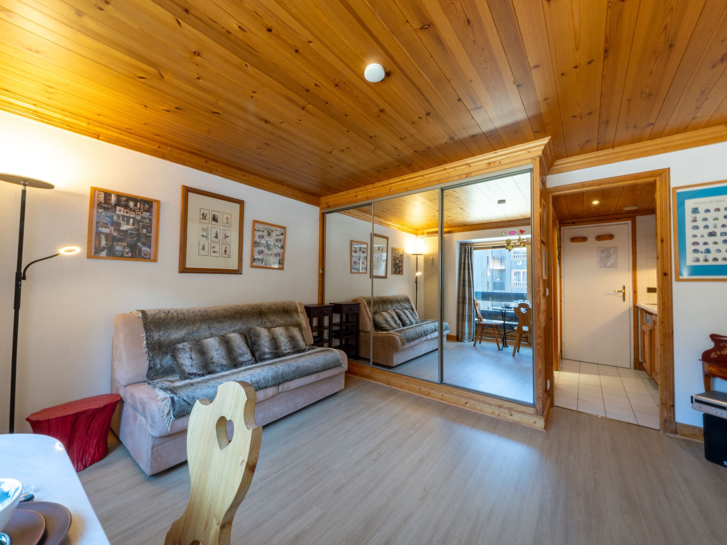 A cozy room with a wooden ceiling, a sofa, a dining table, and a mirror reflecting the dining area.