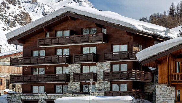 A multi-story wooden building with balconies, stone walls, and snow-covered surroundings.