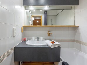 A bathroom with a white sink, a mirror, a towel, and a shelf with toiletries. - Cozy, Well-Maintained Apartment at the Foot of the Slopes with Parking (Val-d'Isère)