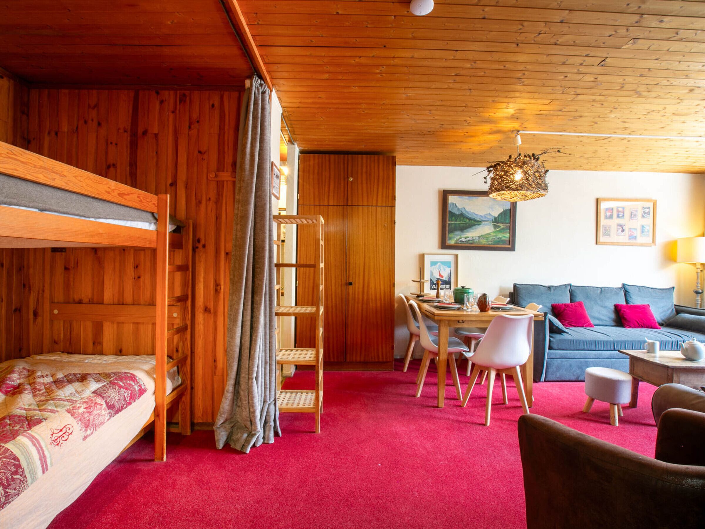 A cozy room with a bunk bed, a dining table with chairs, a sofa, and a red carpet.
