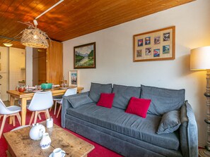 A cozy living room with a grey sofa, red cushions, a wooden coffee table with teapots, and a dining area with a wooden table and chairs. - Cozy apartment for 6, near slopes and center (Val-d'Isère)