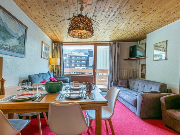 A cozy room with a wooden ceiling, a dining table set for two, a sofa, and a television.
