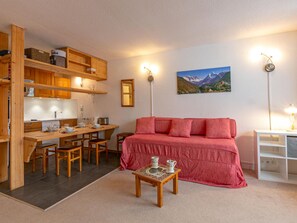 Un espacio habitable compacto con kitchenette, comedor, sofá y un cuadro de montañas en la pared.