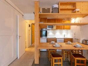 Cocina compacta con armarios de madera, horno empotrado y una zona de comedor con taburetes.