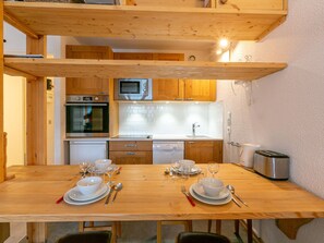 A modern kitchen with wooden cabinets, a microwave, oven, and dishwasher. There is a wooden dining table set with plates, glasses, and cutlery. - Cozy ski-in/ski-out apartment, wifi, pets allowed, parking, 3 pers La Daille (Val-d'Isère)