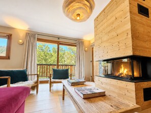Ein gemütliches Wohnzimmer mit Kamin, Holzmöbeln und großen Fenstern.