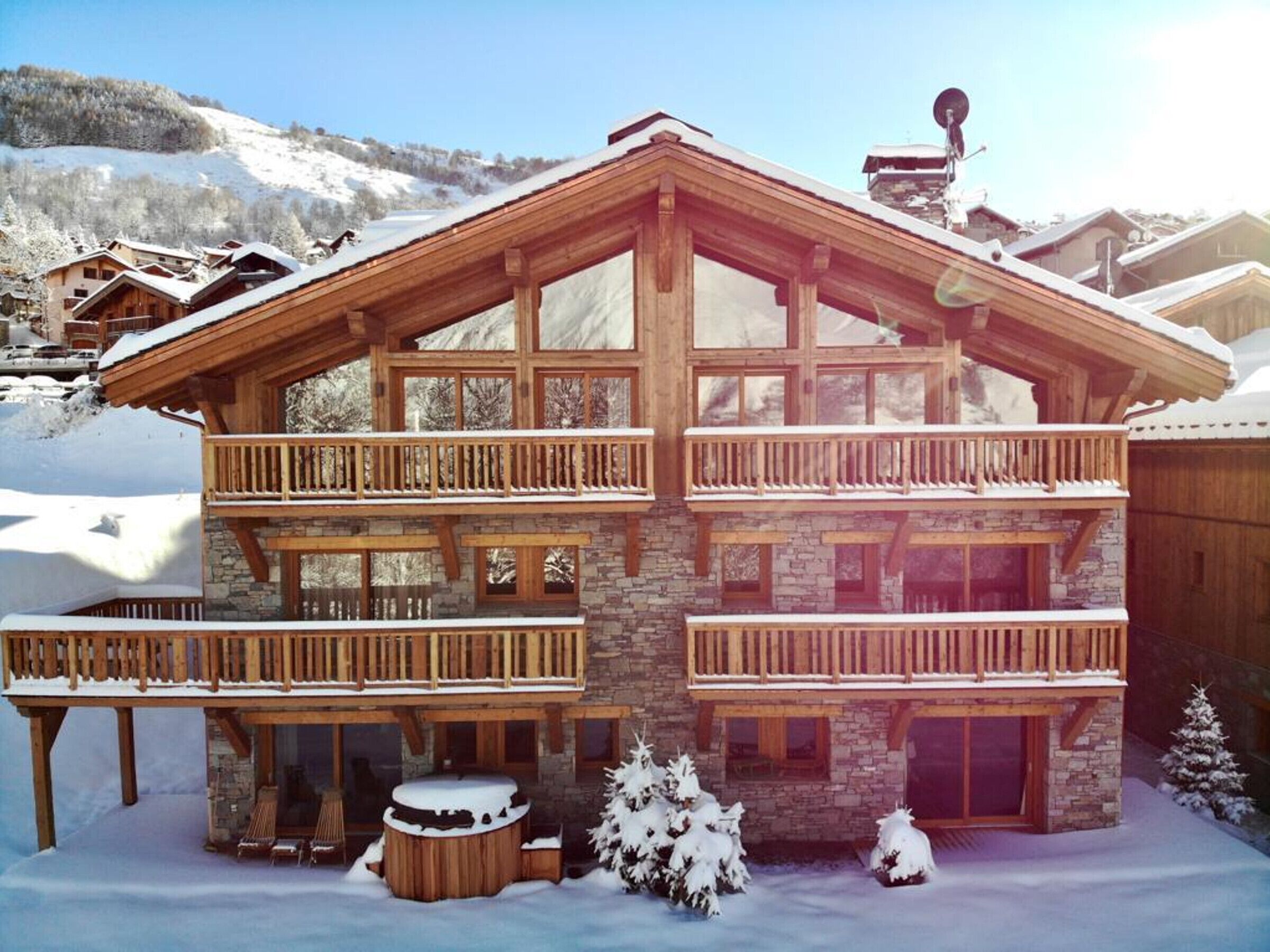 A multi-story wooden chalet with balconies, stone walls, and a snow-covered landscape.