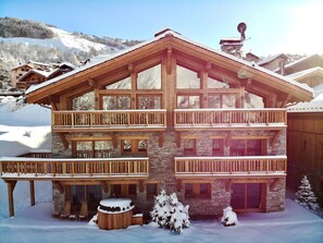 Una cabaña de madera de varios pisos con balcones, muros de piedra y un paisaje cubierto de nieve.