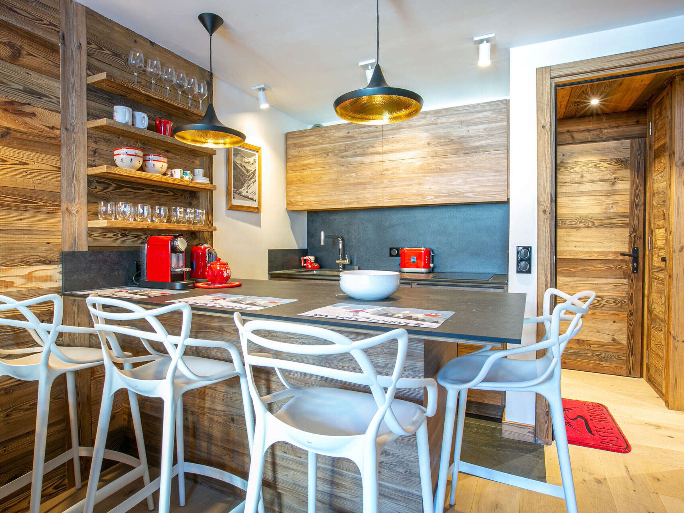 Una cucina moderna con elementi in legno, un'isola centrale con sgabelli da bar e una macchina da caffè rossa.