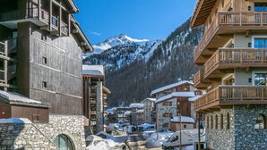 A snow-covered mountain town with wooden buildings, stone walls, and a clear view of a snow-capped mountain in the background.