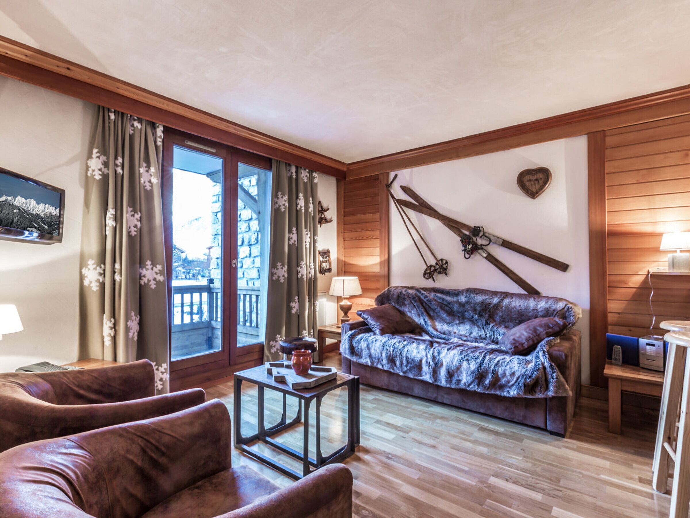 A cozy living room with a wooden ceiling, a sofa, a coffee table, and a view of a balcony.