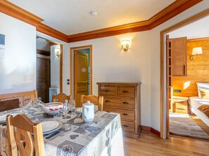 A dining area with a table set for four, wooden chairs, a wooden cabinet, and a wall-mounted light fixture. - Charming 2-room apartment with WIFI in the heart of Val-d'Isère (Val-d'Isère)
