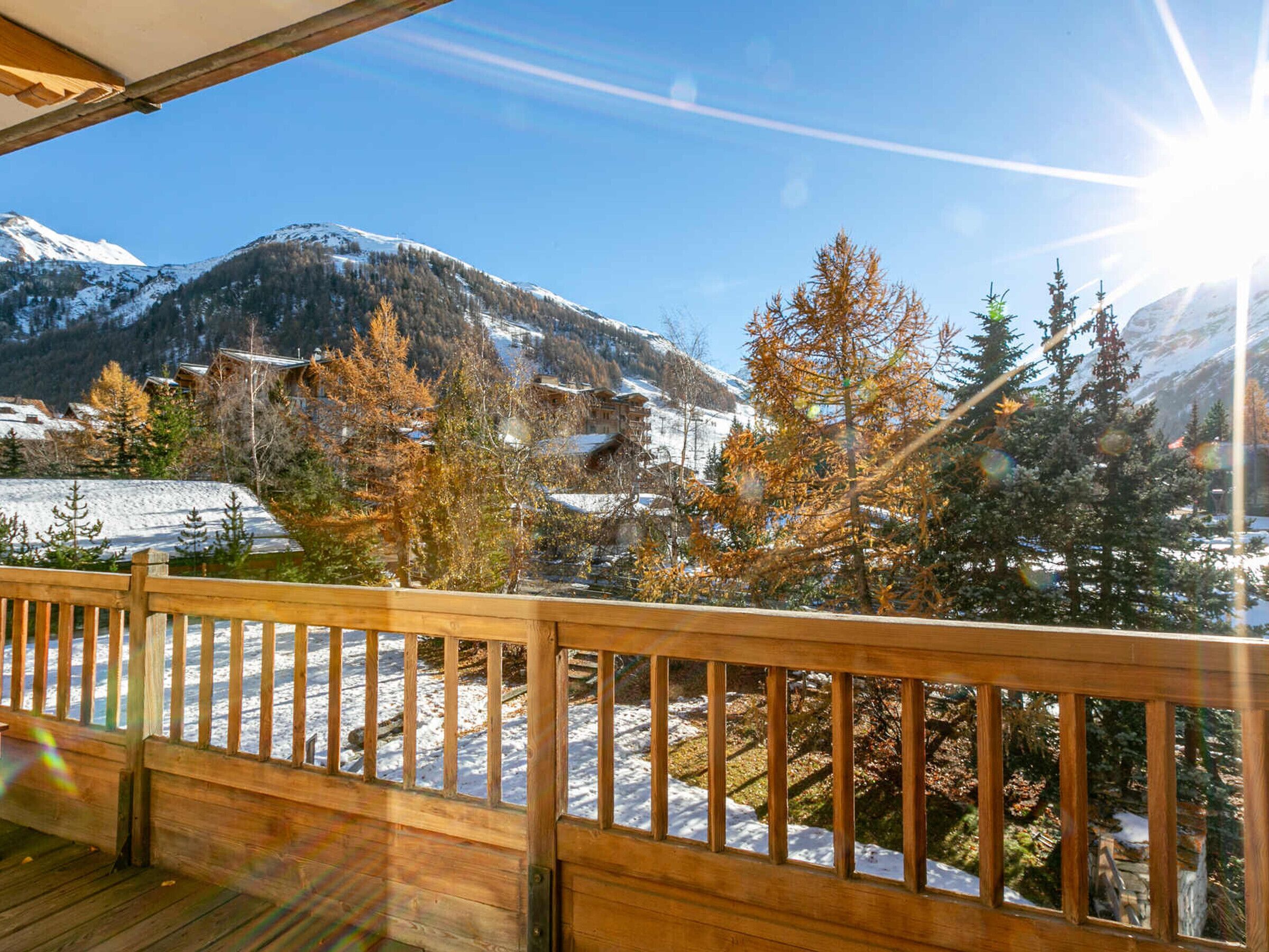A wooden deck with a view of a snowy mountain landscape and autumn-colored trees.