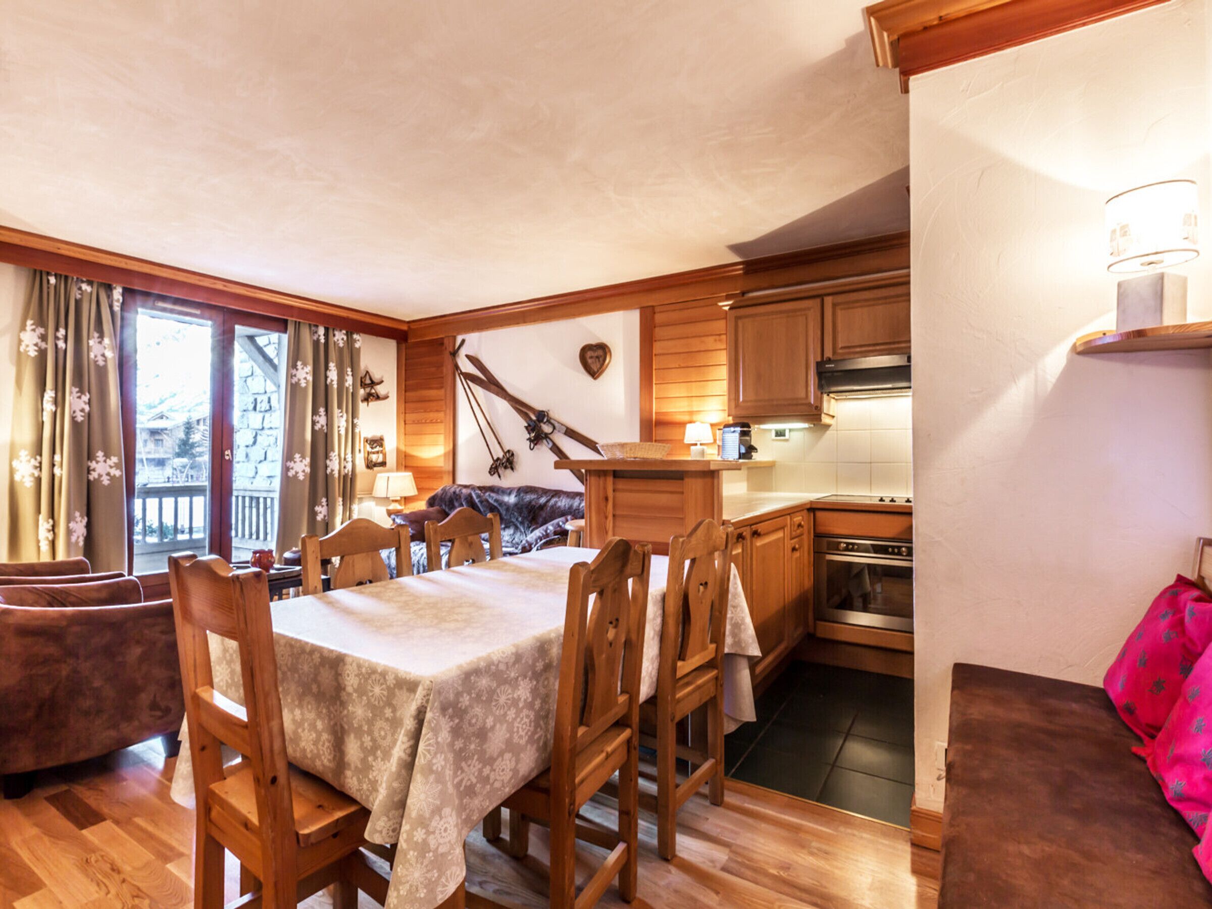 A cozy chalet with a dining area, wooden furniture, a kitchen, and a balcony with curtains.