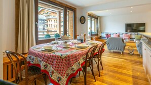 A dining area with a table set for four, large windows, a sofa, and a television in a living area. - Charming, Spacious Apartment with WiFi at the Foot of the Slopes in the Heart of the Resort (Val-d'Isère)