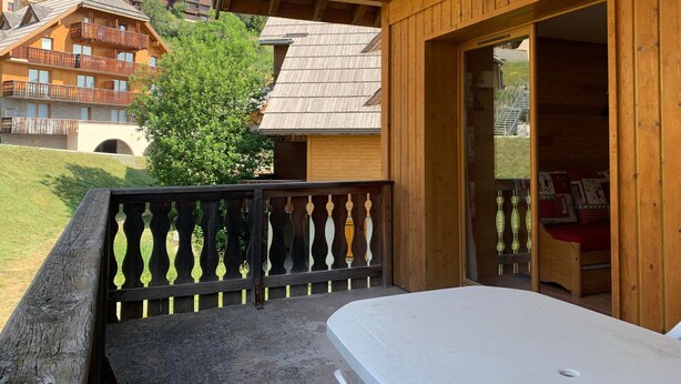 A wooden balcony with a mattress on the floor, a wooden railing, and a view of other buildings in the background. - 28m² Mountain studio for 4 with balcony in Pra-Loup (Pra-Loup)