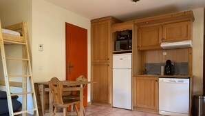 A compact kitchen with wooden cabinets, a white refrigerator, a dishwasher, and a coffee maker on the countertop. - 28m² Mountain studio for 4 with balcony in Pra-Loup (Pra-Loup)