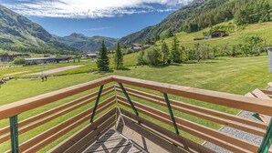 A wooden staircase leading to a terrace with a view of a mountainous landscape and a small village.