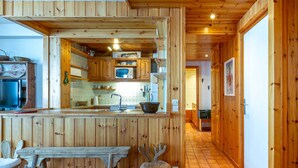 Un interior de madera con una zona de cocina, una mesa de comedor y una silla rústica.