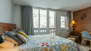Un dormitorio con cama, una silla, ventana con cortinas y vista a un paisaje nevado.