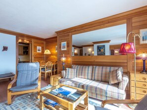 A cozy room with a wooden sofa, a blue chair, a wooden table with magazines, and a wooden cabinet. - Bright studio with WiFi near the slopes (Val-d'Isère)
