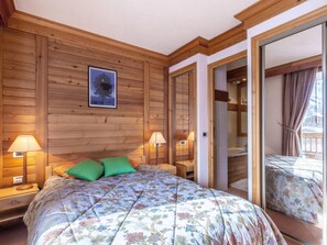 A wooden room with a bed, two bedside lamps, and a framed picture on the wall.