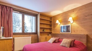 A cozy bedroom with a large bed, wooden walls, a window with curtains, a radiator, and a desk with a chair. - Exquisite and Cozy Apartment with WiFi and Garage in Val-d'Isère (Val-d'Isère)