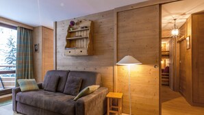 A cozy living room with a sofa, a small side table, a floor lamp, and a wooden wall unit with shelves. - Exquisite and Cozy Apartment with WiFi and Garage in Val-d'Isère (Val-d'Isère)